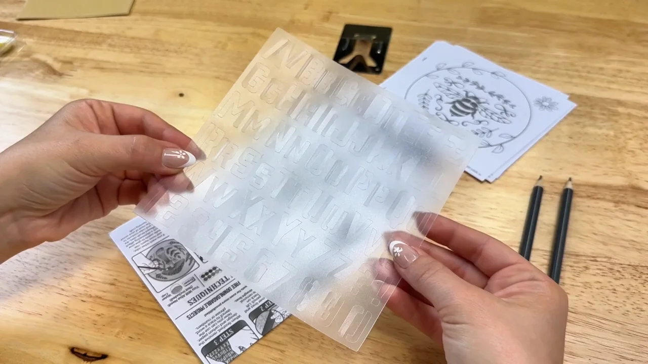 Hands holding a letter stencil beside paper patterns and pencils
