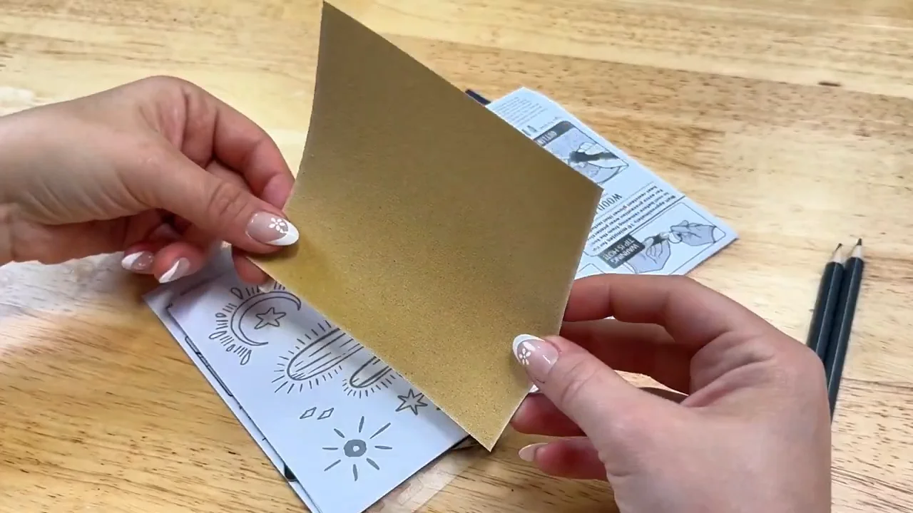 Sandpaper held above printed patterns with pencils on a wooden workbench