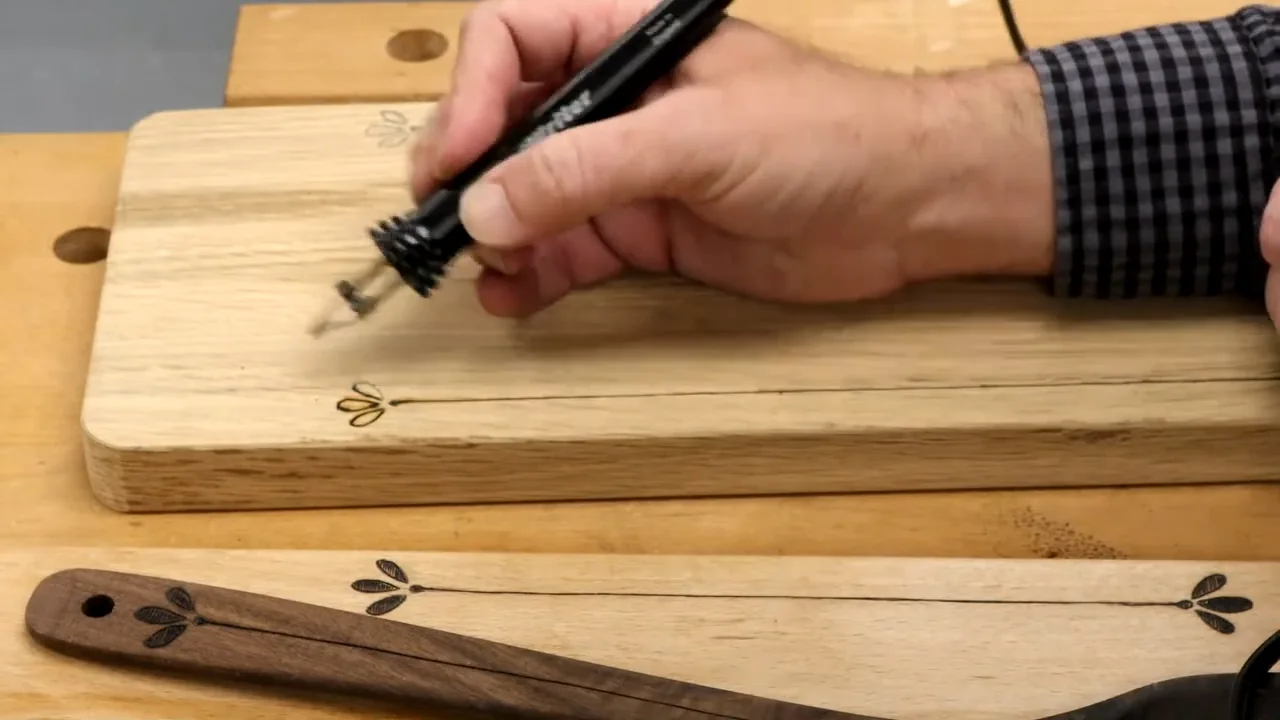 A woodburning pen beside a small leaf motif at the edge of a serving board