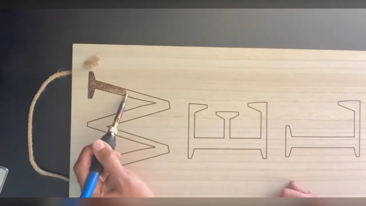 Wood-burning pen filling an outlined letter on a wooden welcome sign