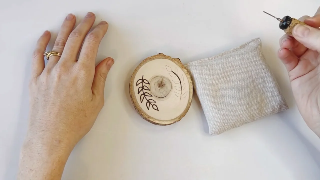 A leaf design being burned onto a round wooden coaster
