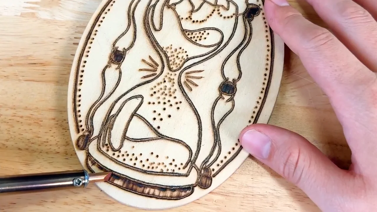 Adding burned details to a decorative hourglass design on an oval wood plaque