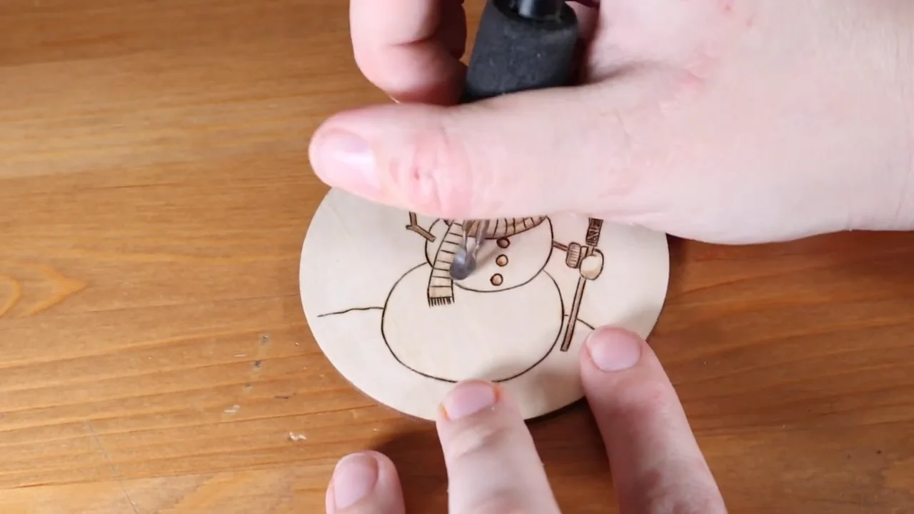 A pyrography pen adds detail to a snowman ornament