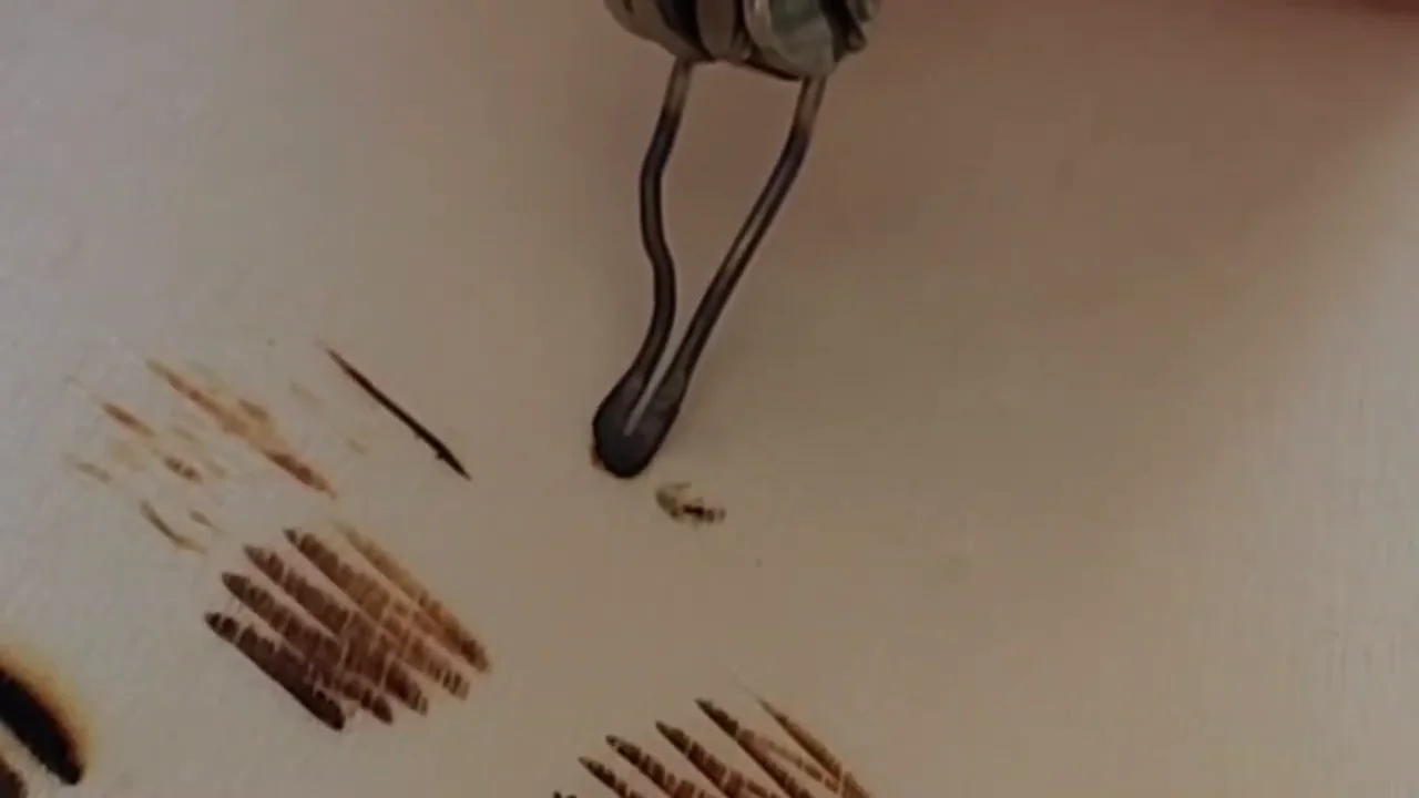 Close-up of a wire shading nib beside pale and darker practice strokes on wood