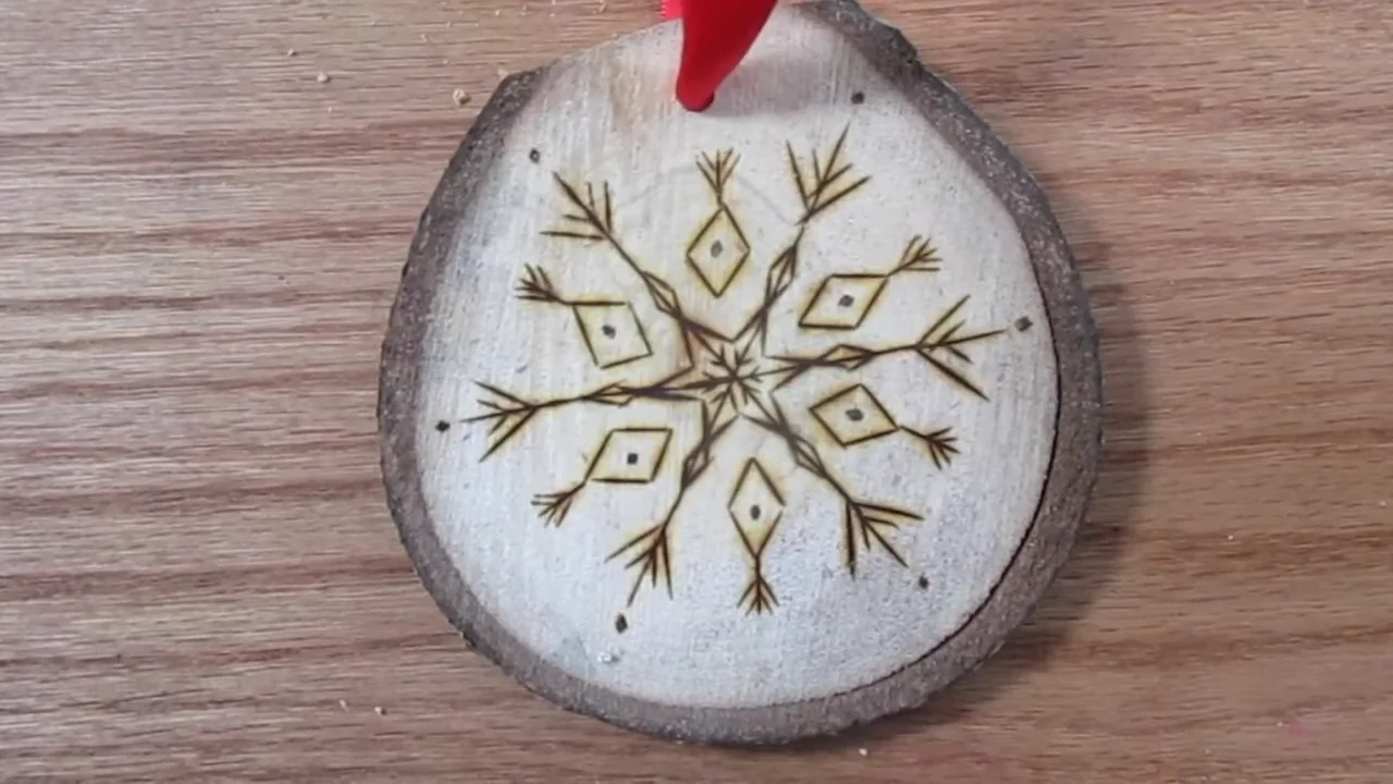 A wood-burned snowflake ornament on a bark-edged slice with a red ribbon hanger.