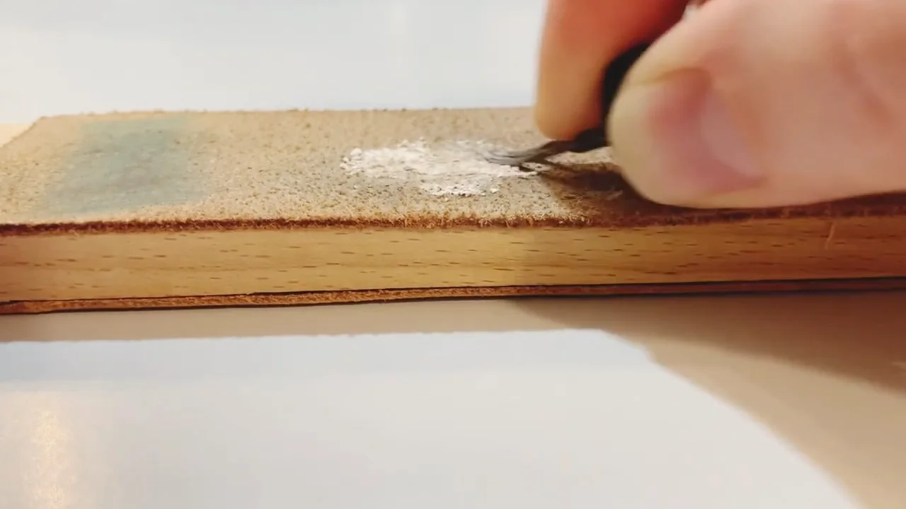 Close-up of a pyrography tip resting against a leather strop during cleaning